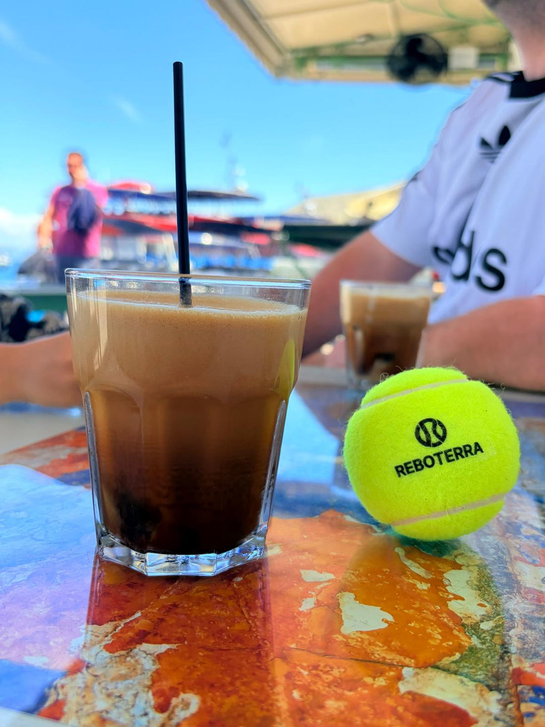 Iced coffee and a Reboterra padel ball at Symi marina